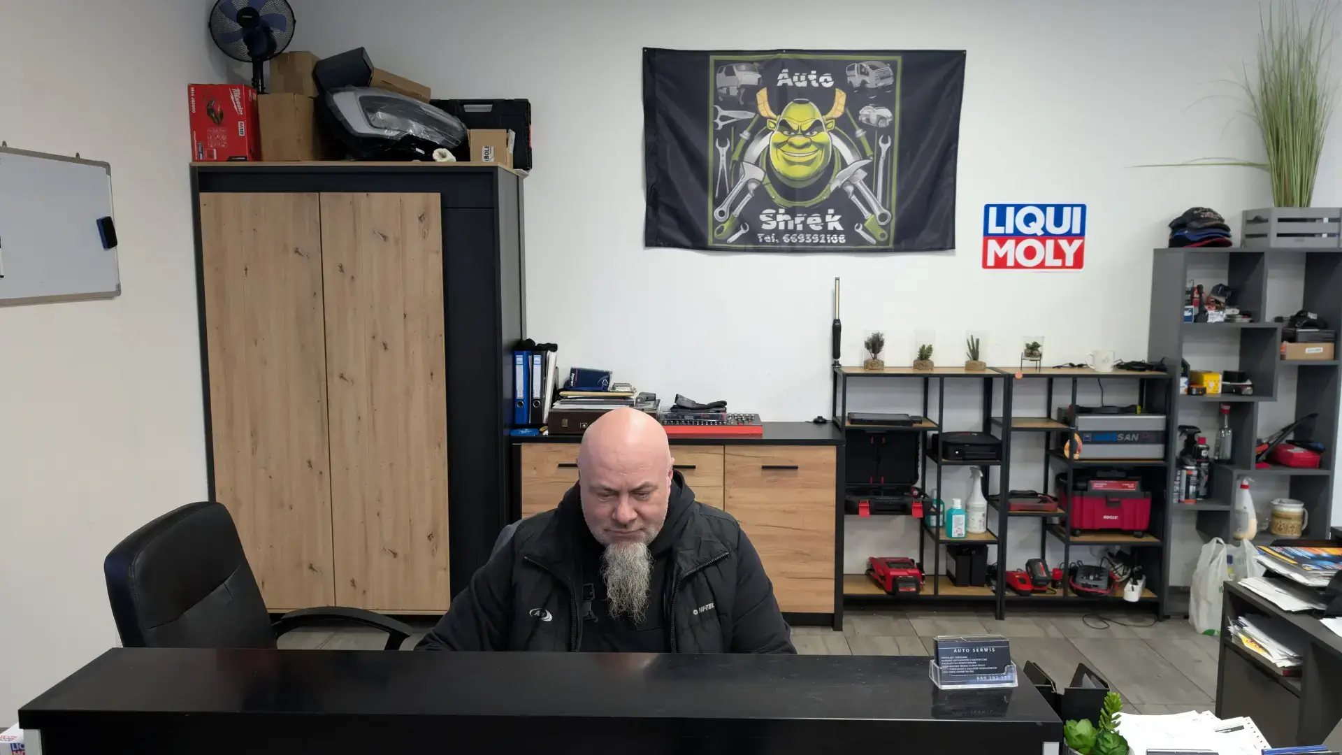 Właściciel warsztatu samochodowego Autoshrek w biurze obsługi klienta w Szczecinie na tle firmowego baneru i logo Liqui Moly.