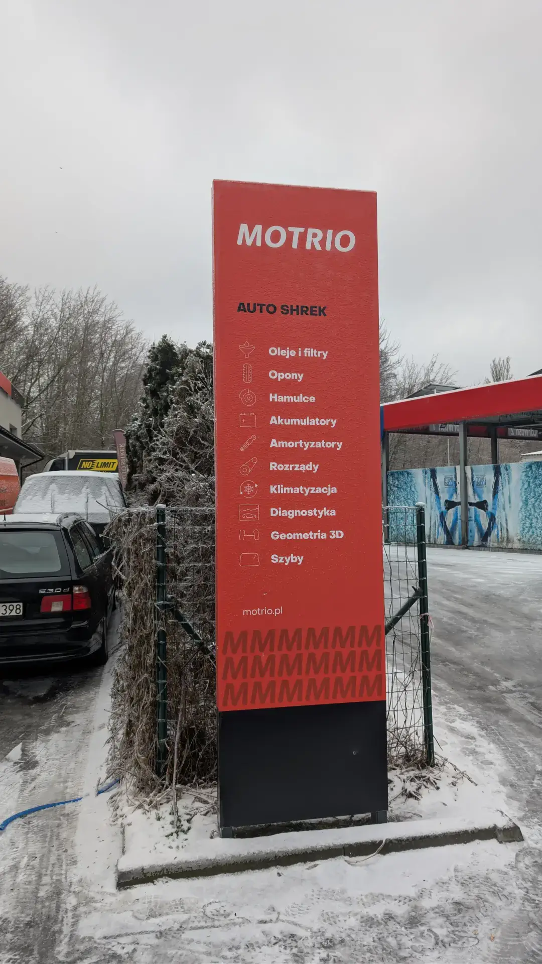 Czerwony pylon reklamowy warsztatu Autoshrek z ofertą napraw: rozrządy, diagnostyka i serwis szyb.