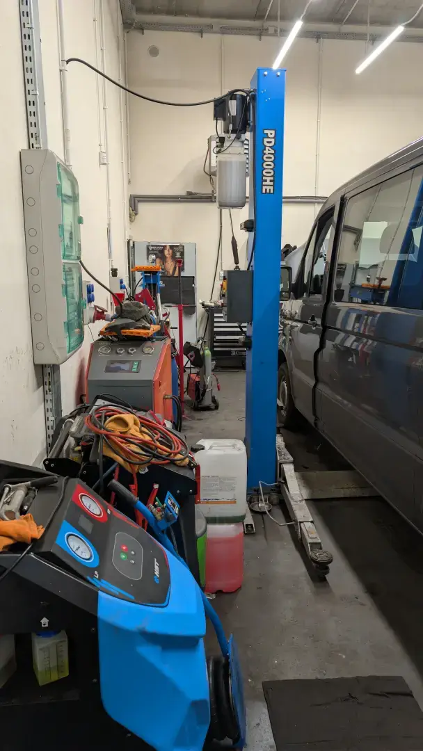 Stacja do serwisu i nabijania klimatyzacji samochodowej na tle stanowiska naprawczego.